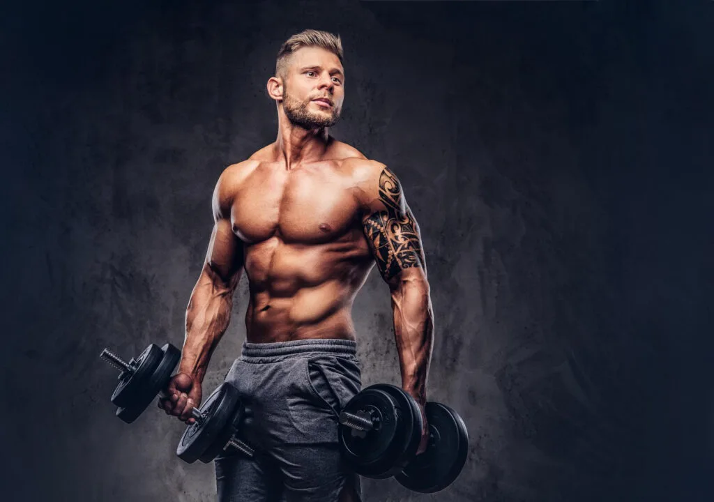 powerful stylish bodybuilder with tattoo his arm doing exercises with dumbbells isolated dark background https://healthyhabitforlife.com/wp-content/uploads/2023/08/portrait-muscular-man-taking-break-hydrate-his-body-after.jpg - https://healthyhabitforlife.com